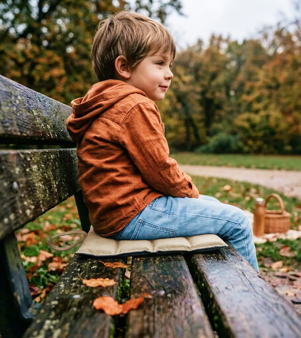 Junge sitzt auf dem NELARO Sitzkissen auf einer Parkbank im Herbst