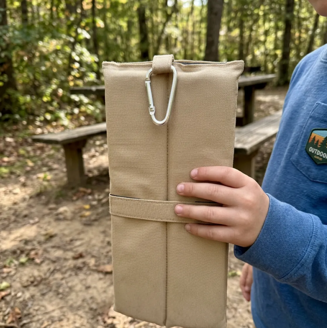 Kinderhand hält das gefaltete NELARO Sitzkissen mit Karabiner